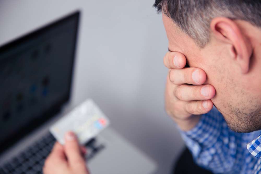 Upset man holding credit card with laptop on background