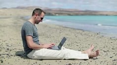 stock-footage-happy-man-with-modern-laptop-sitting-on-the-beach